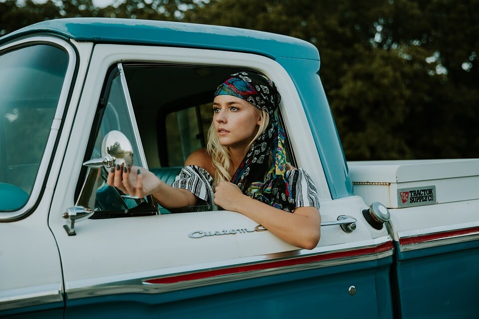 Chica rubia mirándose al espejo del auto antes de viajar por las vacaciones de Semana Santa